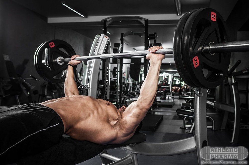 Выполняет жим штанги от груди, лежа на скамье